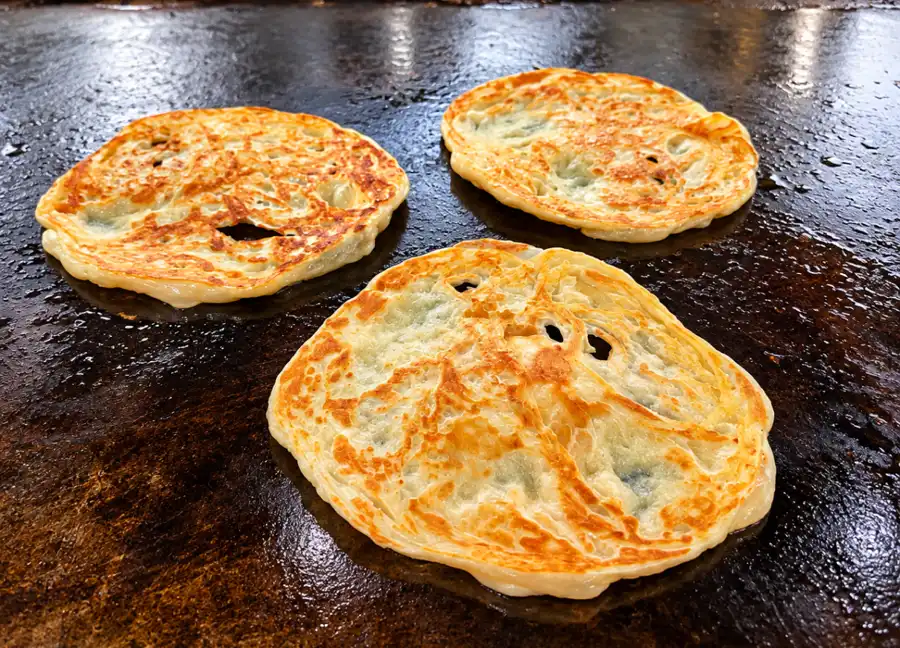 Roti canai dimasak di atas kuali leper panas di sebuah kedai makan Kampung Baru