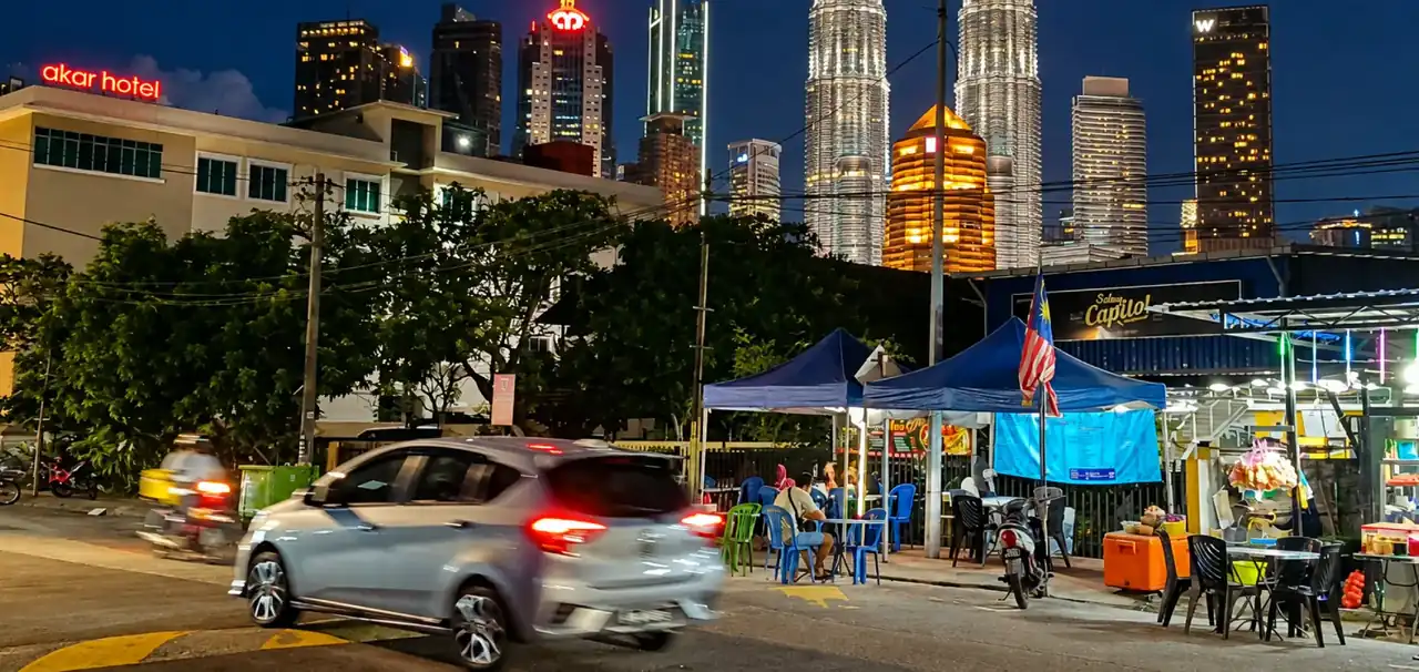 Jalan di Kampung Baru pada waktu malam berhampiran Akar Hotel, dengan gerai makanan dan latar langit bandar